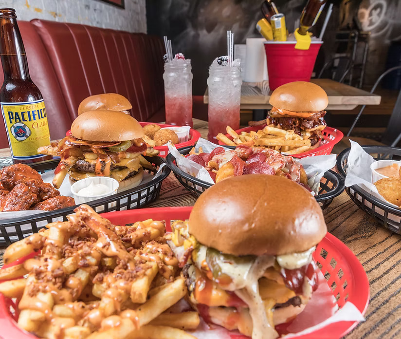 Several gourmet burgers, fries, and other bar food on a table.