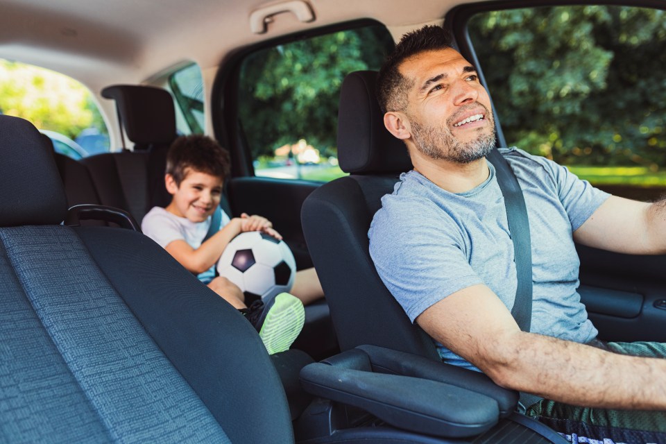 A father and son smiling in a car, the son holding a soccer ball.