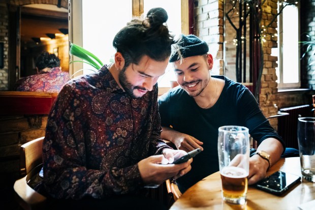 Two hipsters looking at a smartphone together at a bar.