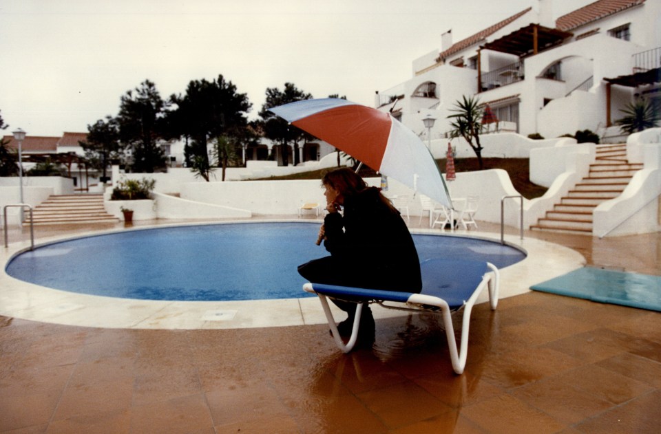 A publicity officer sits under an umbrella by a pool on the set of the British soap opera *Eldorado*.