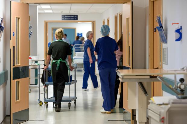 Busy NHS hospital corridor with medical personnel and equipment.