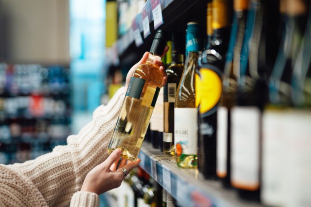 Woman's hand selecting a bottle of white wine from a supermarket shelf.