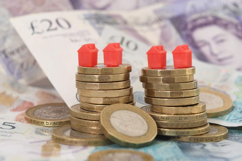 Three small red houses atop stacks of British coins, resting on banknotes.