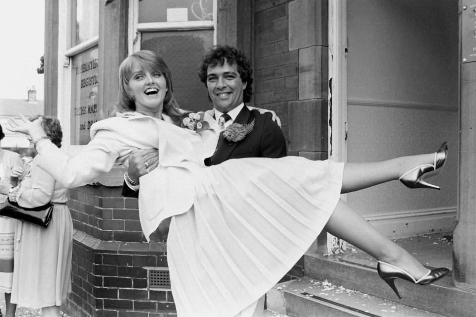 Black and white photo of Linda Nolan being carried by her husband Brian Hudson after their wedding.