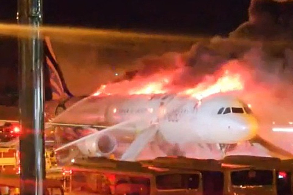 Nighttime scene of a large fire with smoke and emergency vehicles.