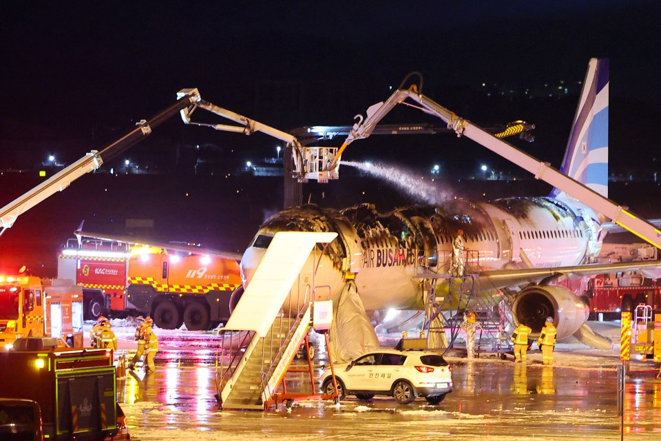 Firefighters extinguishing a fire on an Air Busan airplane at an airport.