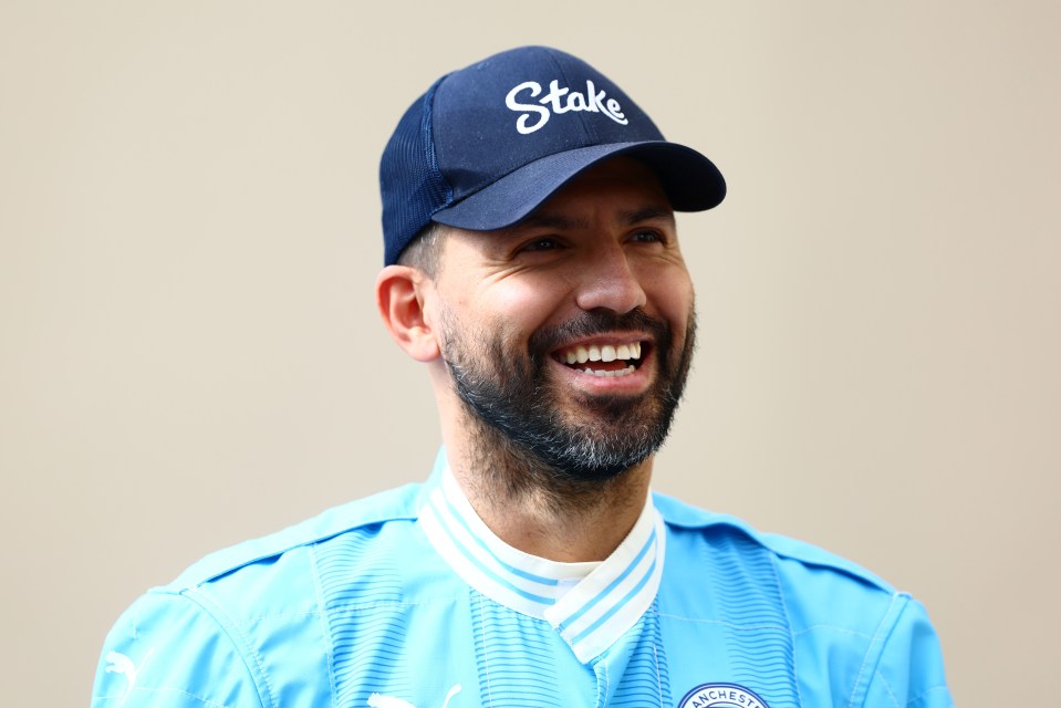 Sergio Aguero smiling and wearing a light blue shirt and a "Stake" baseball cap.