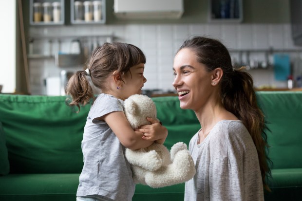 Smiling mother and daughter playing with a teddy bear.