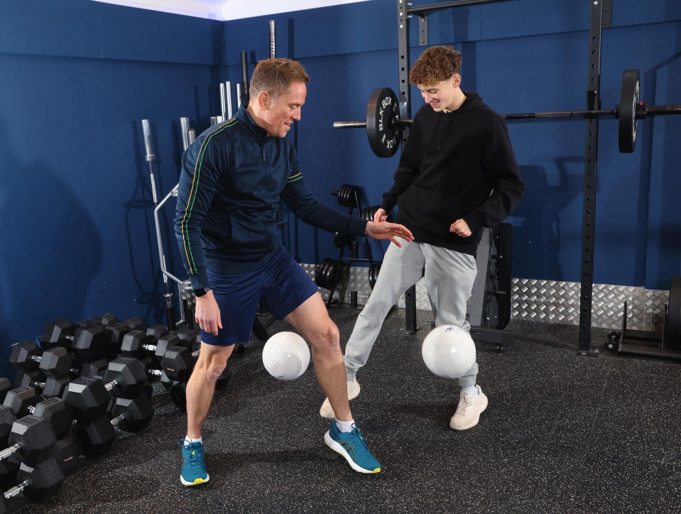 Two men juggling soccer balls in a gym.