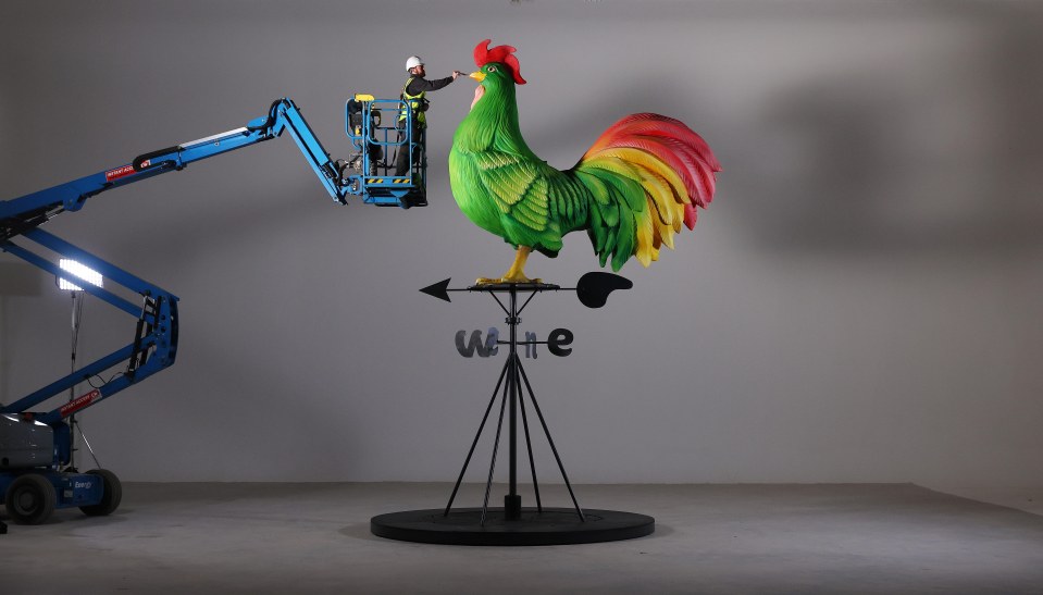 A worker on a lift installing a large rooster weathervane.