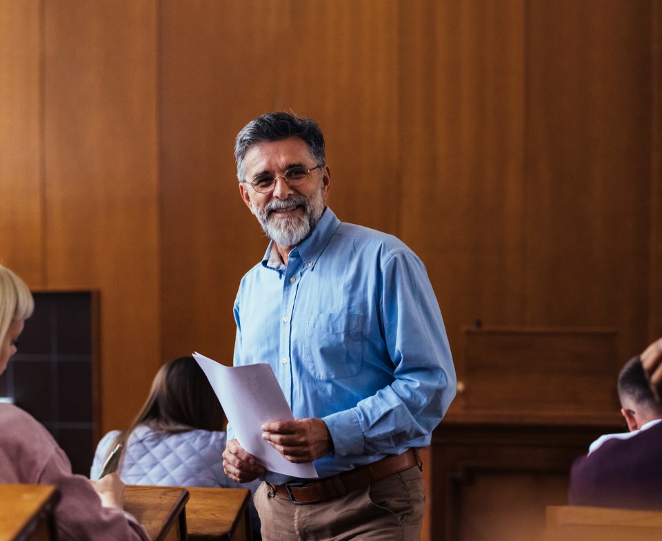 Smiling professor holding papers in a university classroom.