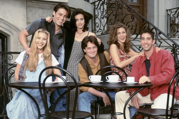 The six main actors from the TV show Friends sitting at outdoor cafe tables.