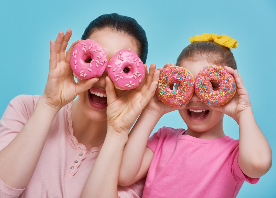 Mother and daughter playfully hold donuts in front of their eyes.