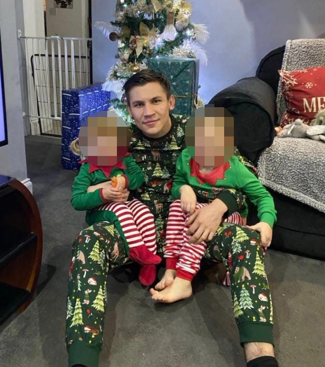 Man in Christmas pajamas holding two young children.