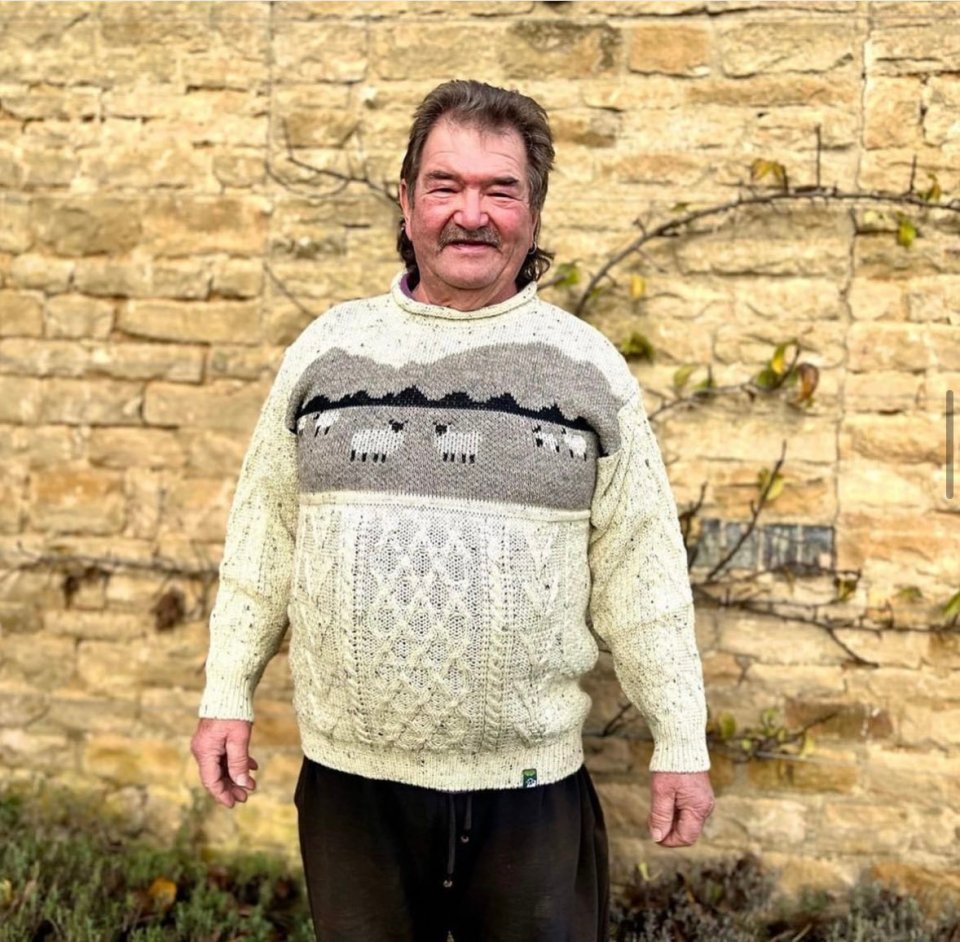 Gerald Cooper, farmer, standing in front of a stone wall.