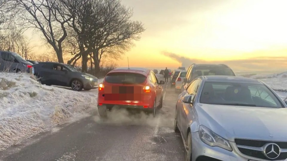 Snow-covered road blocked by parked cars.