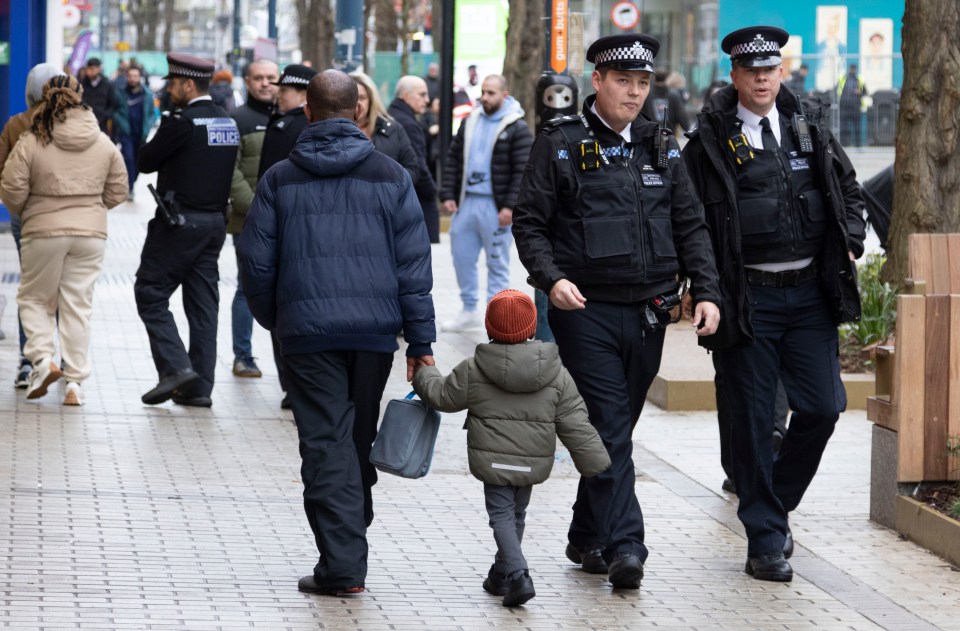 Police officers walking past a man and child in Woolwich.