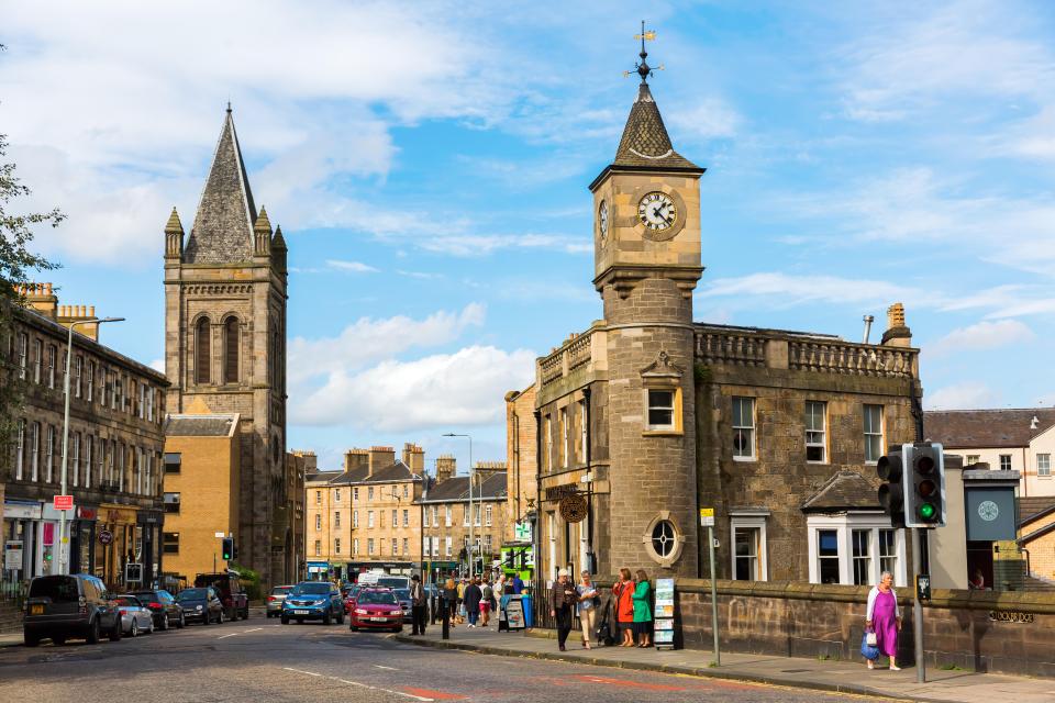 Street view of Stockbridge in Edinburgh, Scotland, showing a clock tower and church spire.