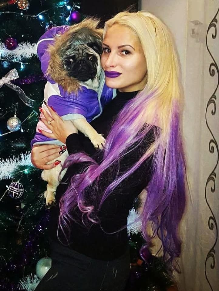 Woman with purple hair holding a pug in a purple jacket.