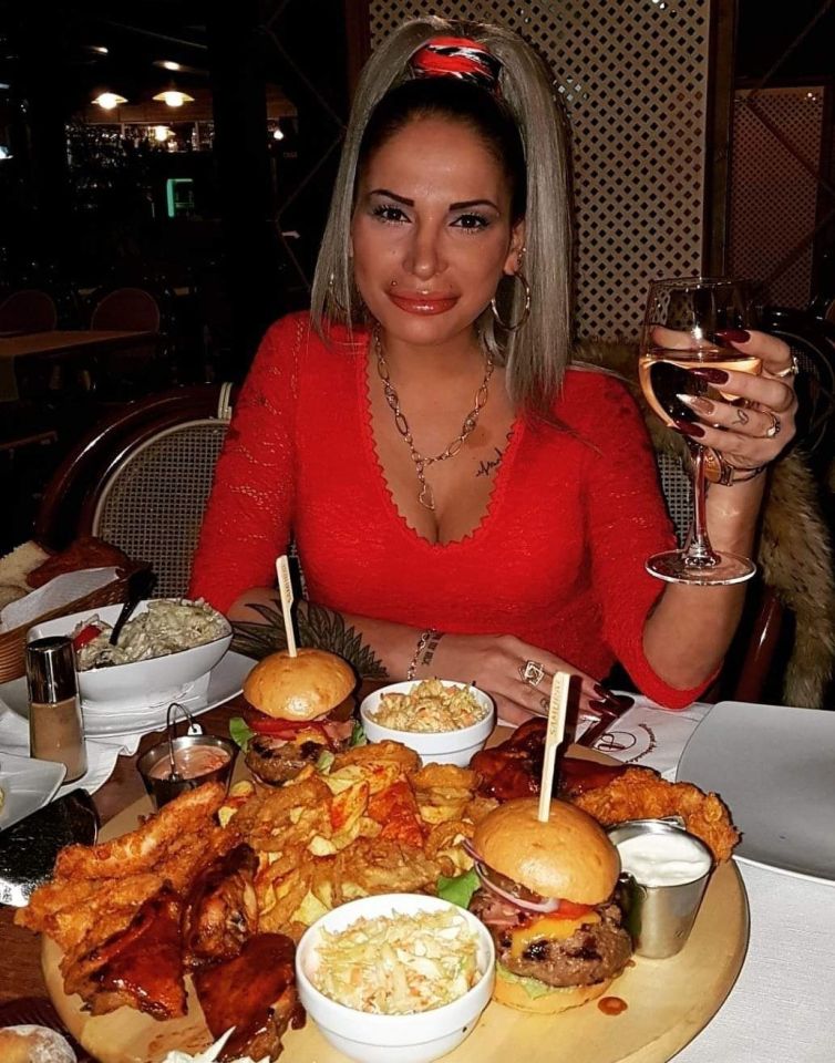 Woman enjoying a large meal with burgers, fries, and coleslaw.