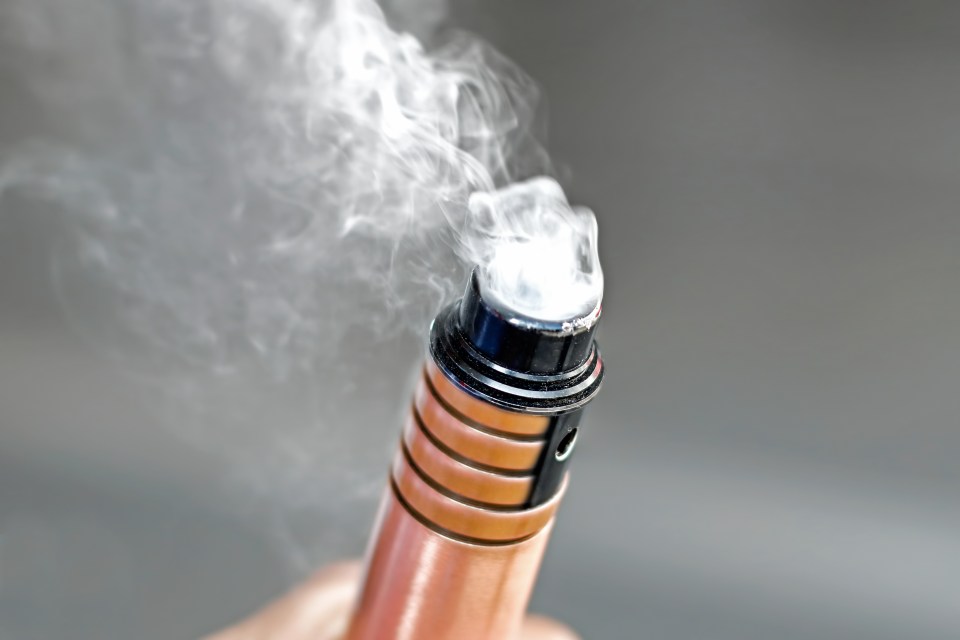 Hand holding an electronic cigarette emitting vapor.