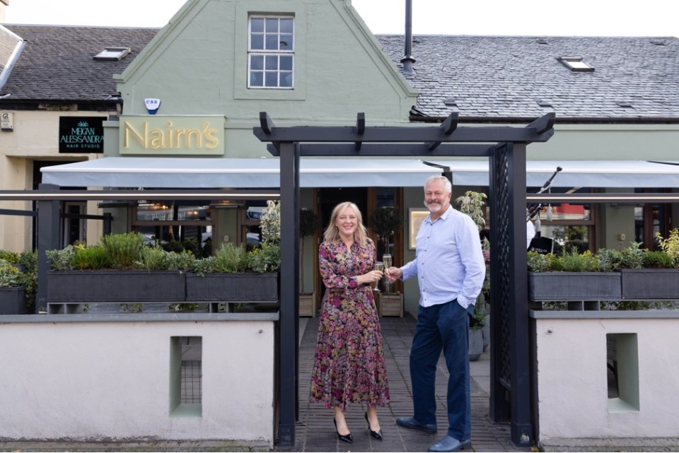 Two people toasting with champagne glasses in front of Nairn's restaurant.