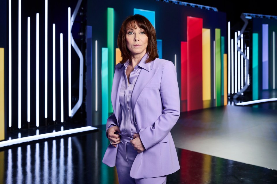 Kay Burley in a lavender suit against a backdrop of colorful bars.