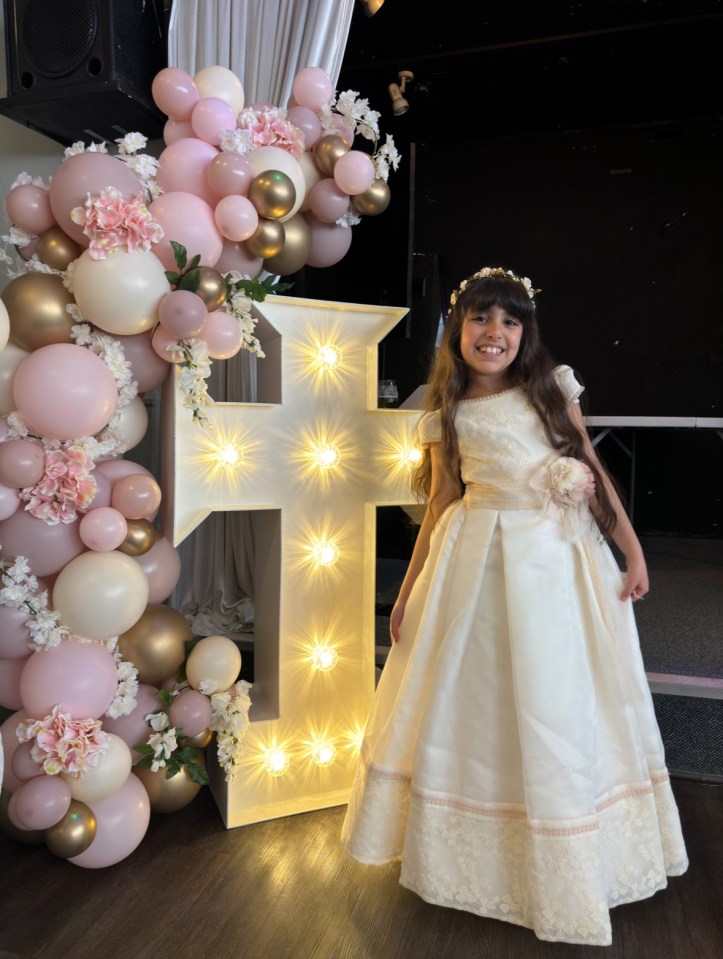 Girl in white dress standing next to a lighted cross.