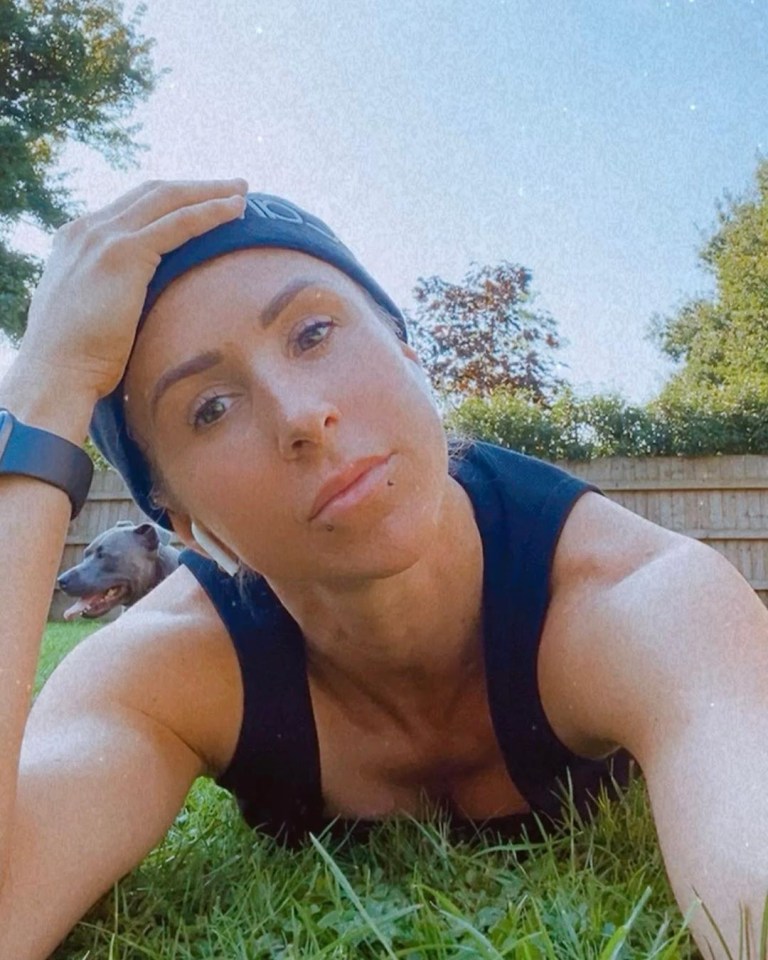 Woman lying on grass in a black tank top with a dog in the background.