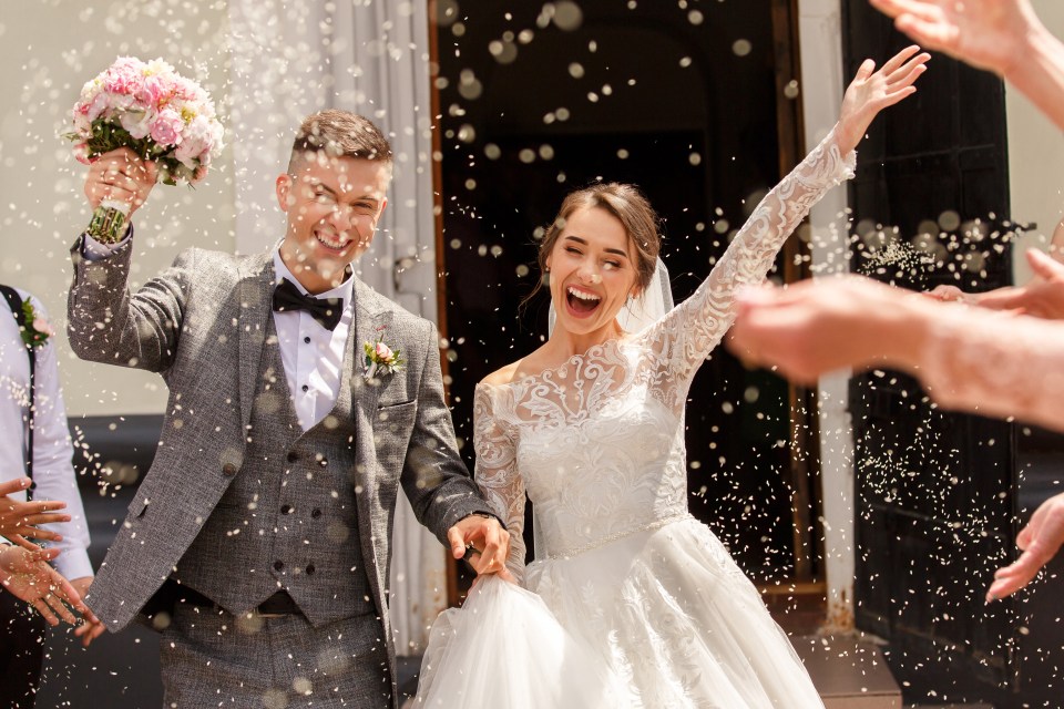 Happy bride and groom exiting their wedding ceremony, showered with rice.