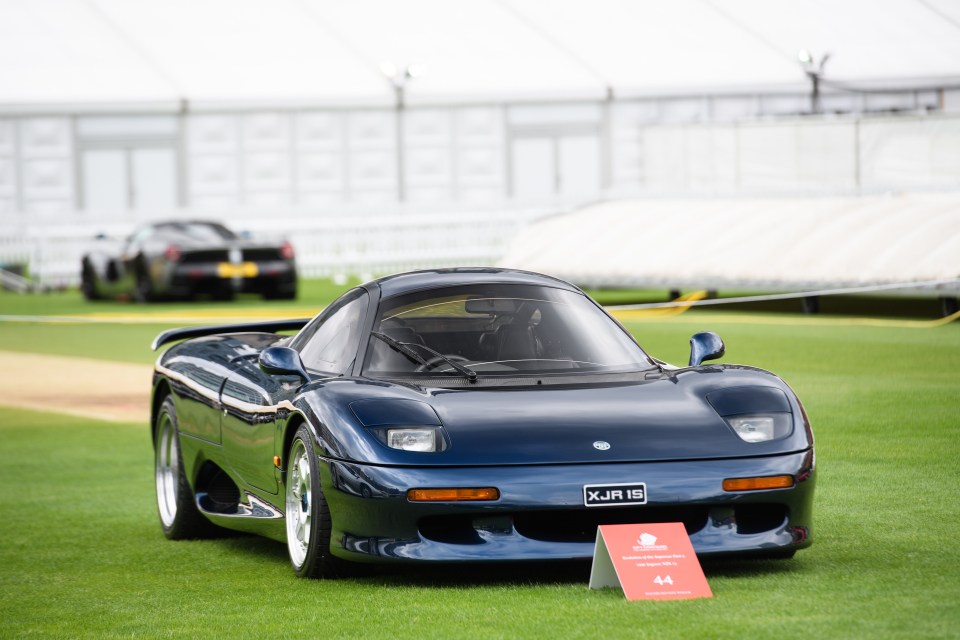 A dark blue Jaguar XJR-15 sports car on a grassy lawn.