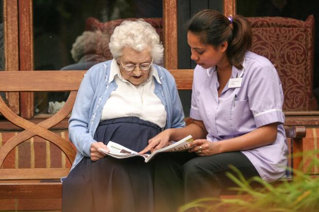 Elderly woman and caregiver reading a magazine together.