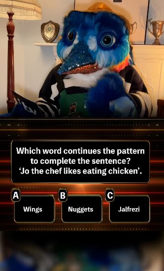 A blue bird puppet participates in a quiz show.  The question asks which word completes the sentence, "Jo the chef likes eating chicken."  The options are wings, nuggets, and jalfrezi.