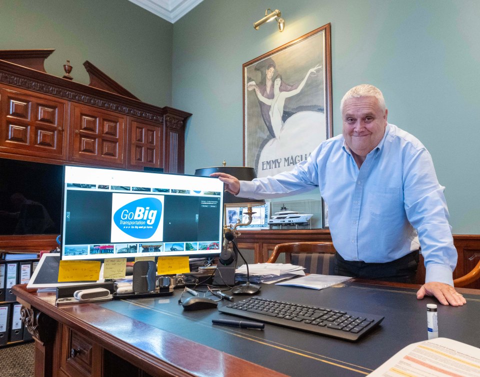 Man in his home office, pointing at a computer screen showing his company logo, GoBig Transportation.