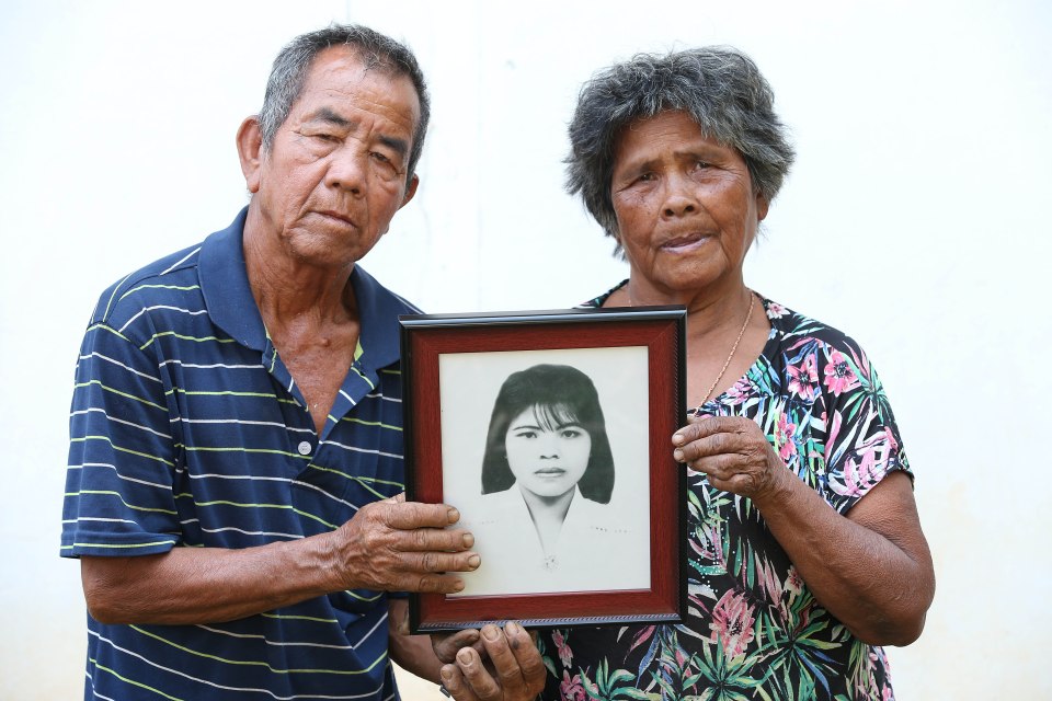 Elderly couple holding a framed photo of their deceased daughter.