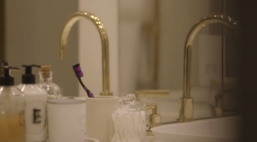 Toothbrush in a bathroom with gold faucets.