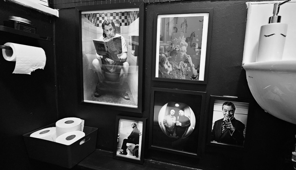 Black and white photos of people on toilets and other framed images decorate a bathroom.