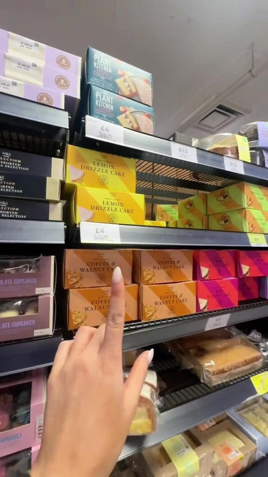 Hand pointing at M&S cakes on a shelf.