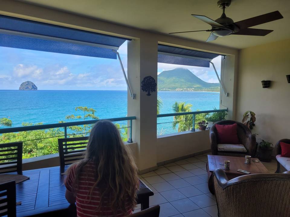 Woman sitting on a balcony overlooking the ocean and a mountain.