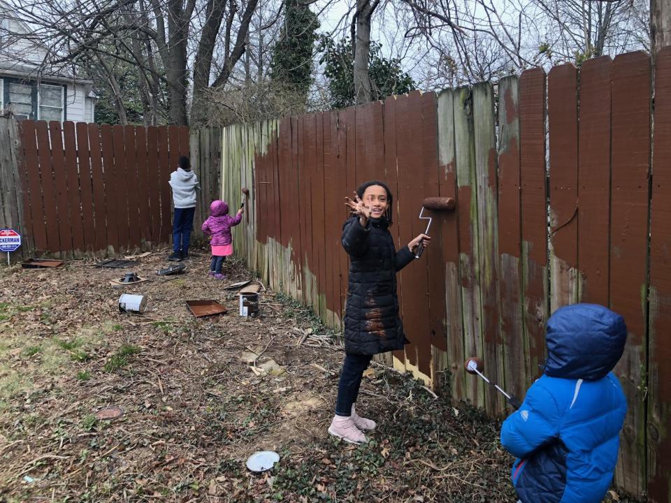 Three children painting a brown wooden fence.