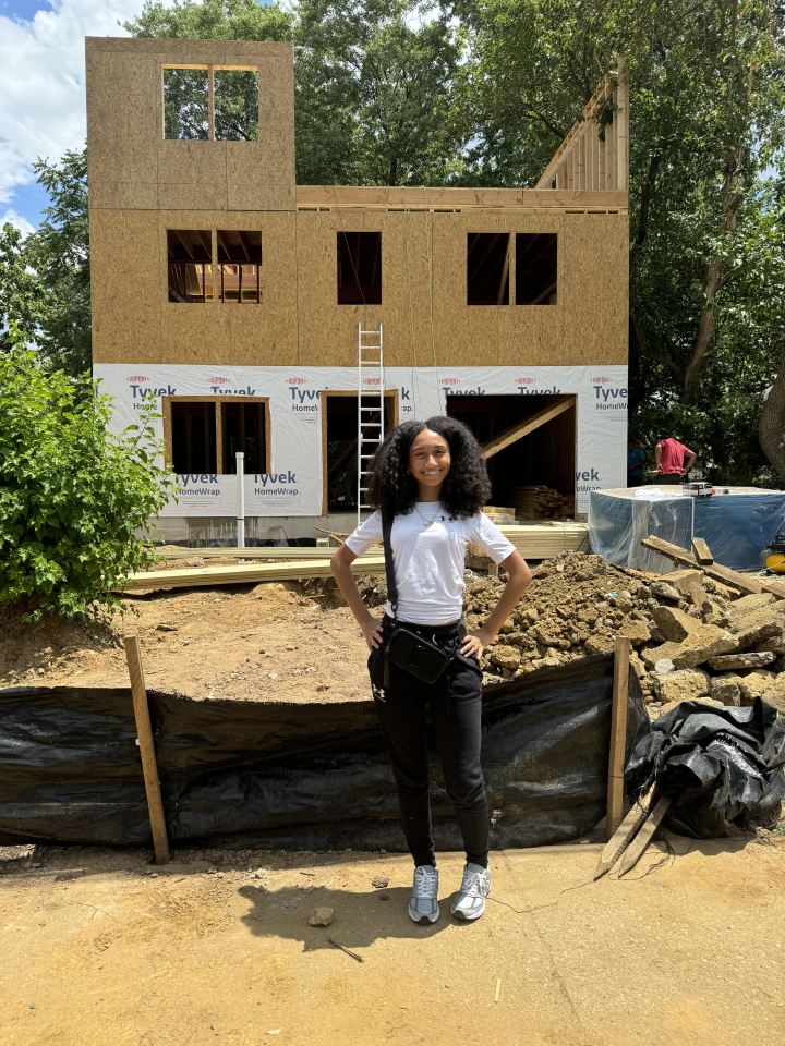 A teenage girl stands in front of a house under construction.