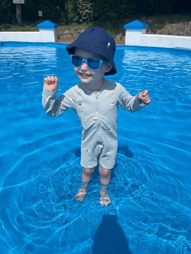 Toddler in a swimming pool wearing a hat and sunglasses.