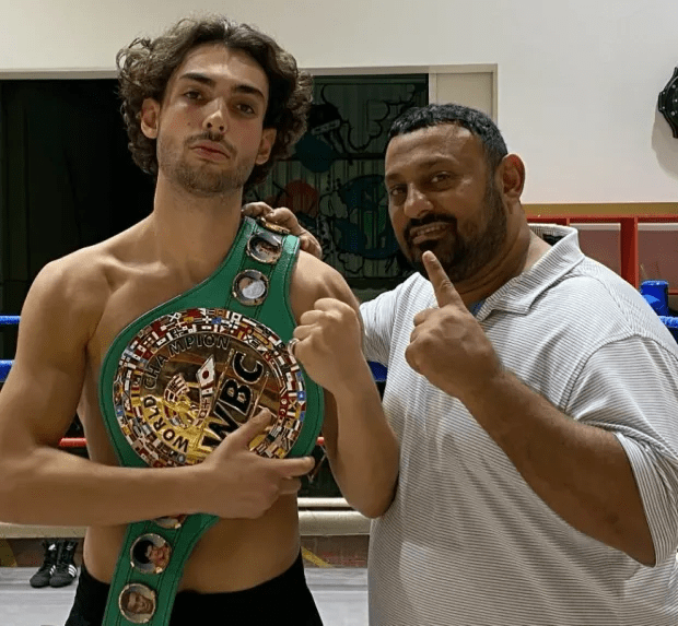 A young boxer holding a WBC world champion belt with his trainer.