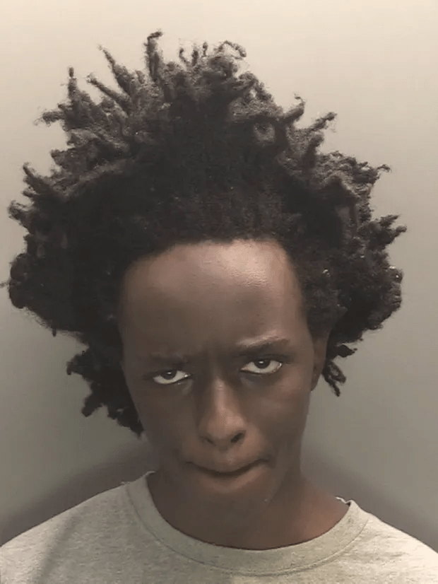 Mugshot of a person with dark skin and short dreadlocks.