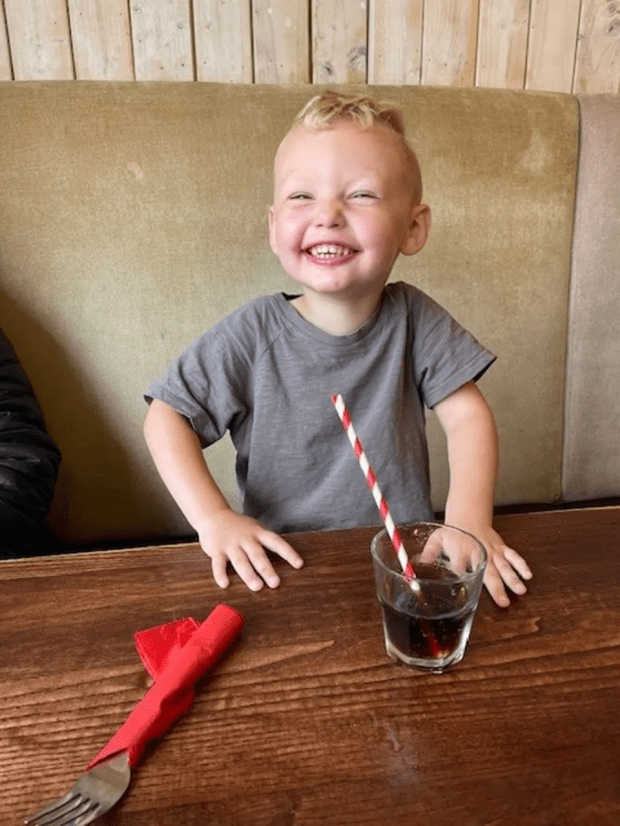 Smiling toddler at a table with a drink.