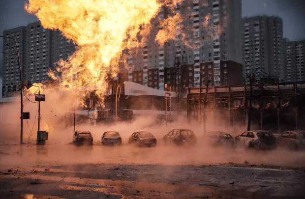 Large fire and smoke engulfing cars and buildings in a city.