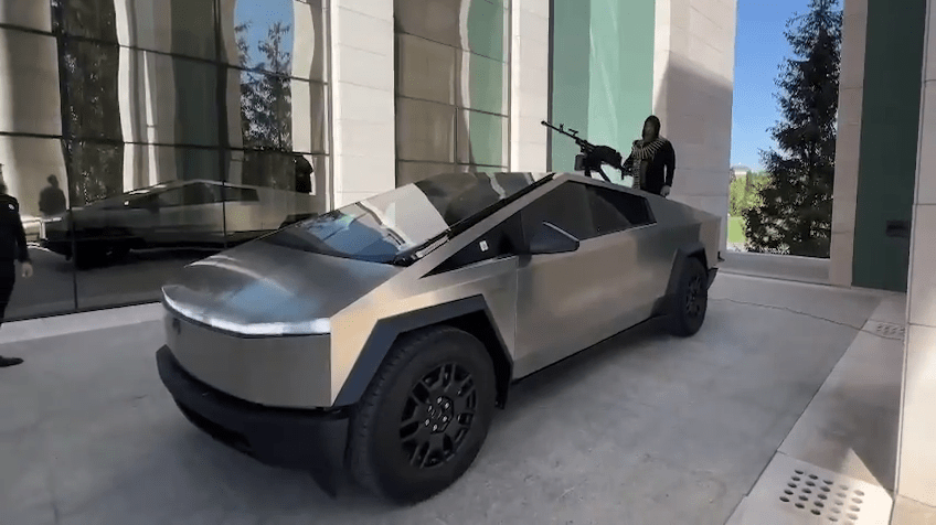 A silver Tesla Cybertruck with a machine gun mounted on the roof.