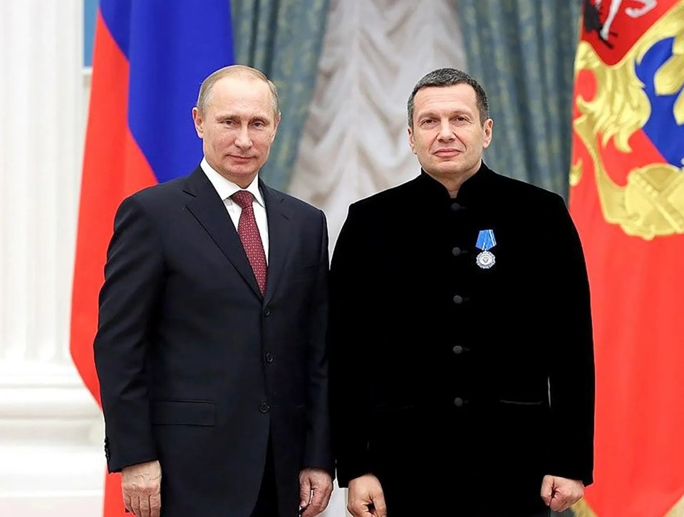 Vladimir Putin and a man in a black jacket receiving an award.