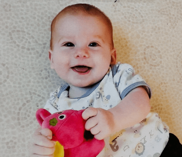 Smiling baby holding a pink stuffed animal.