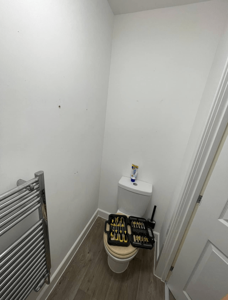 Bathroom with toilet, tools, and towel warmer; walls need repair.